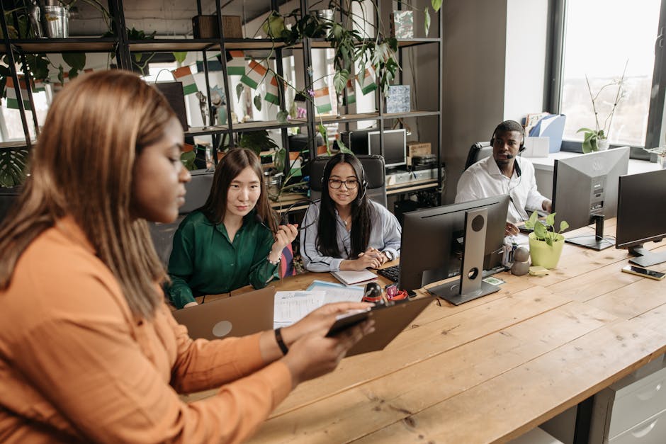 A diverse group of office workers collaborating at a wooden desk in a modern workspace.